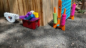 Une boîte en plastique rouge remplie de blocs de construction colorés, un jouet blanc doté d’un écran et une structure de jeu escamotable bleue et orange.
