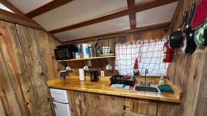 Une cuisine compacte aux murs en bois, avec un petit réfrigérateur, un évier et divers ustensiles et appareils de cuisine.