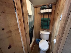 Une petite salle de bain en bois, avec des toilettes, une étagère avec des serviettes et une serviette verte accrochée au mur.