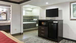 A hotel room with a bed, a TV mounted on the wall, a minibar, and a bathroom visible through an open door. - HomeStay Inn & Suites (Russellville)