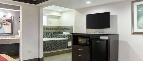 A hotel room with a bed, a TV mounted on the wall, a minibar, and a bathroom visible through an open door.