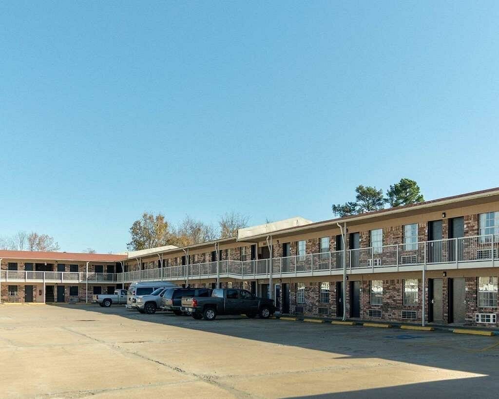 Ein Motel mit zweistöckiger Struktur, mehreren Zimmern und einem Parkplatz.