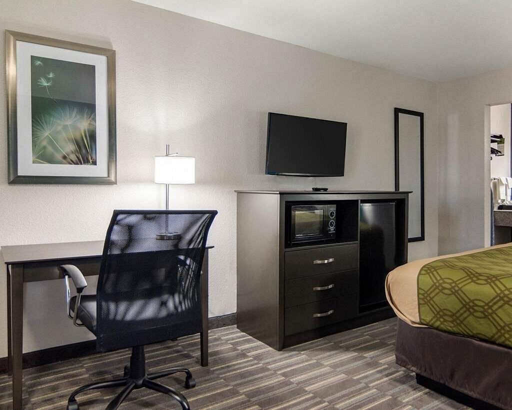 Ein Hotelzimmer mit Schreibtisch, Stuhl, Fernseher, Minibar und Bett.