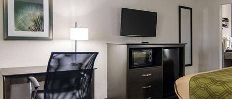 Ein Hotelzimmer mit Schreibtisch, Stuhl, Fernseher, Minibar und Bett.