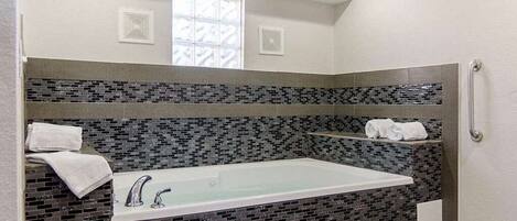 A modern bathroom with a large bathtub, a tiled backsplash, and a window above the sink.
