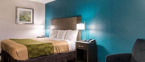 Una habitación de hotel con cama, mesita de noche, lámpara y una silla.