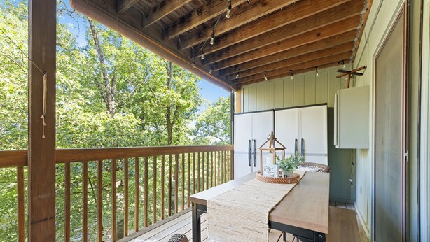 Une terrasse en bois avec une table et des chaises, une vue sur les arbres et un bâtiment à l’extérieur blanc.