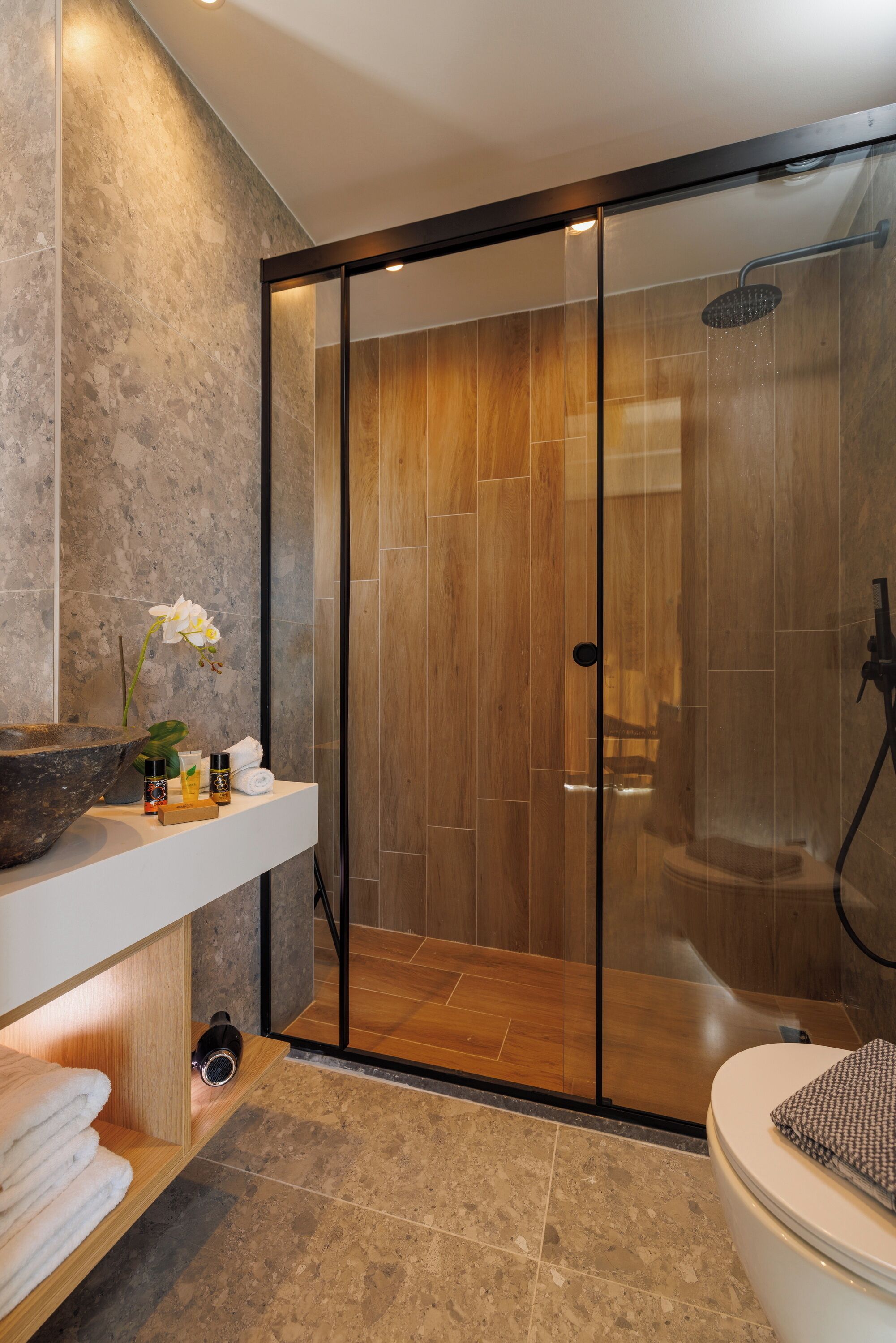 A modern bathroom with a glass-enclosed shower, a wooden vanity, and a marble-tiled floor.