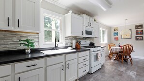 A modern kitchen with white cabinetry, a black countertop, a stove, and a dining area with a table and chairs.