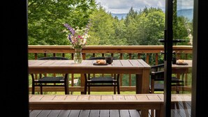 Una terraza de madera con una mesa y sillas, un florero con flores y vistas a un paisaje boscoso.