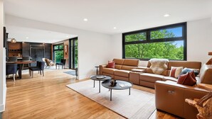 Una sala de estar moderna con un gran ventanal, un sofá, una mesa de centro y un comedor con sillas y una mesa.
