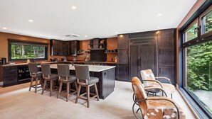 Una cocina moderna con armarios de madera oscura, una isla central con taburetes y un amplio ventanal con vistas al exterior.