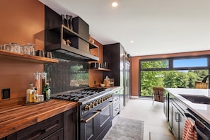 A modern kitchen with a large stove, wooden shelves, and a view of the outdoors.
