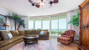 A spacious living room with a large sectional sofa, a round coffee table, and a striped armchair. There is a large window offering a view of the outdoors. - Phenomenal Gulf Views From This Three Bedroom, Three Bathroom Condo. Complimentary Boat Slip! (Orange Beach)