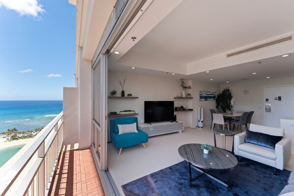 Ein modernes Wohnzimmer mit Balkon und Meerblick, einem Flachbildfernseher und einem Essbereich.