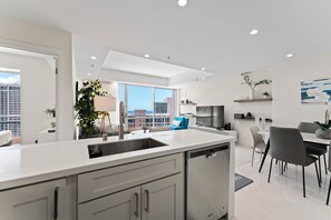 Eine moderne Küche mit einer großen Kochinsel, einem Essbereich mit Tisch und Stühlen sowie Blick auf die Stadt durch große Fenster.