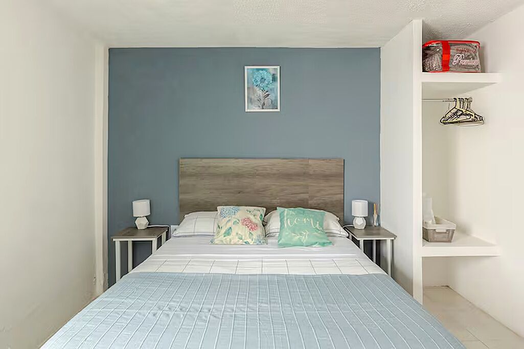 Quarto com cama, mesas de cabeceira, encosto de cama, prateleira na parede e quadro emoldurado.