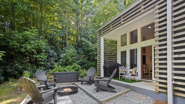 An outdoor patio with Adirondack chairs, a fire pit, and a grill area. - Prize-Winning Modern Home in the Mountains (Boone)