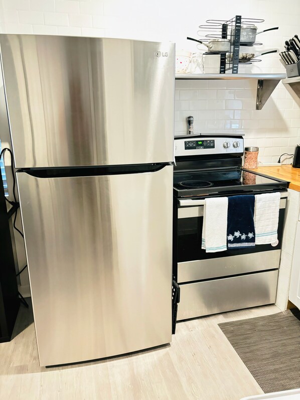 A kitchen with a stainless steel refrigerator, a stove, and a microwave. There are pots and pans on a rack above the stove.