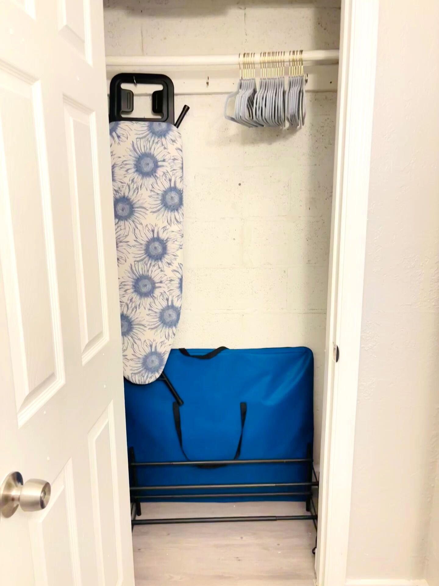A small, enclosed space with a blue fabric item on a rack, a white door, and a wall with a subtle texture.