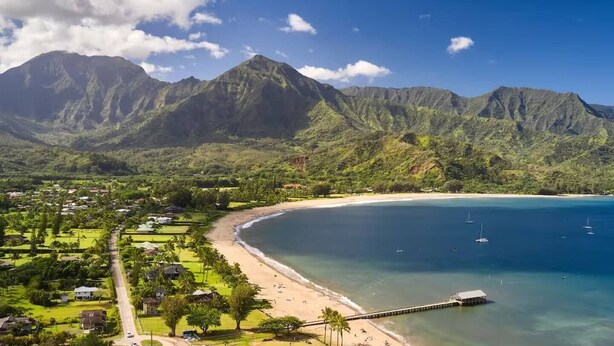 Un paysage côtier avec une plage, une eau d’un bleu limpide et des montagnes en arrière-plan.