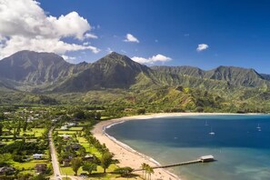 Un paysage côtier avec une plage, une eau d’un bleu limpide et des montagnes en arrière-plan.