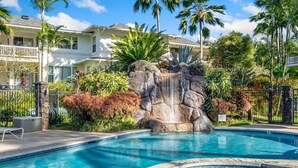 Une piscine agrémentée d’une cascade, entourée de plantes tropicales et bordée d’un immeuble à plusieurs étages.