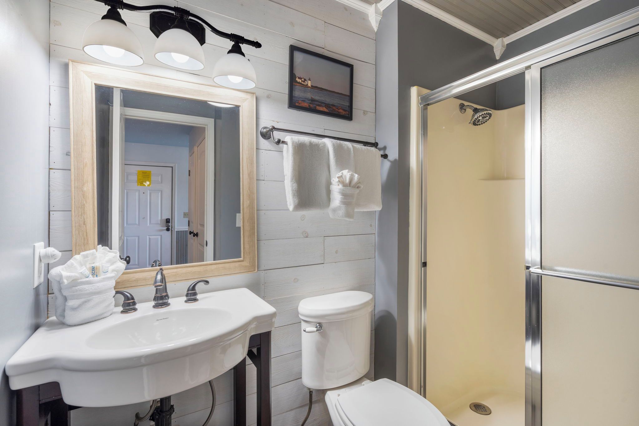 A bathroom with a white sink, a toilet, a shower enclosure, and a mirror with three lights.