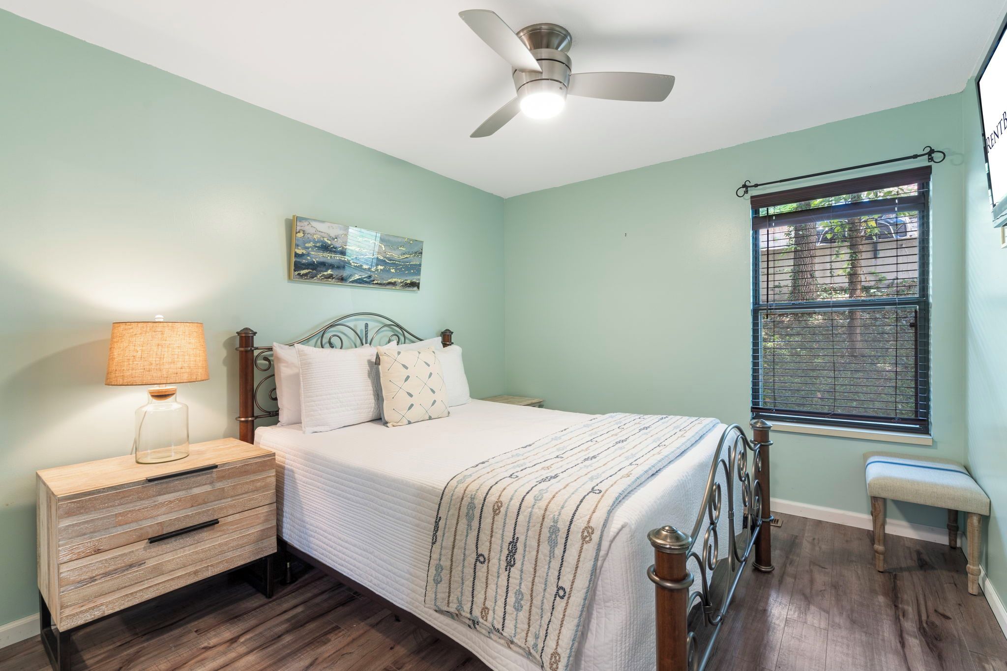 A bedroom with a bed, bedside table, lamp, and a window with a view.