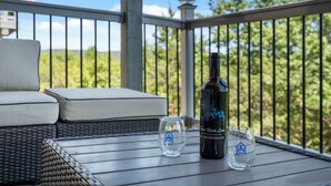 Un balcón con mobiliario de mimbre, una botella de vino y dos copas sobre una mesa de madera.