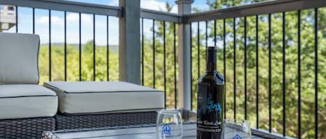 A balcony with wicker furniture, a bottle of wine, and two glasses on a wooden table.