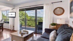 Una sala de estar con sofá, mesa de centro, televisor y balcón con vistas.