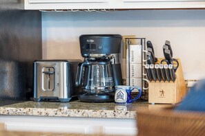 Una encimera de cocina con cafetera, tostadora, taza y bloque de cuchillos.