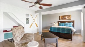 Un dormitorio con cama, ventilador de techo, una obra de arte en la pared y una escalera.