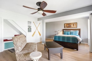 A bedroom with a bed, a ceiling fan, a wall-mounted artwork, and a staircase.