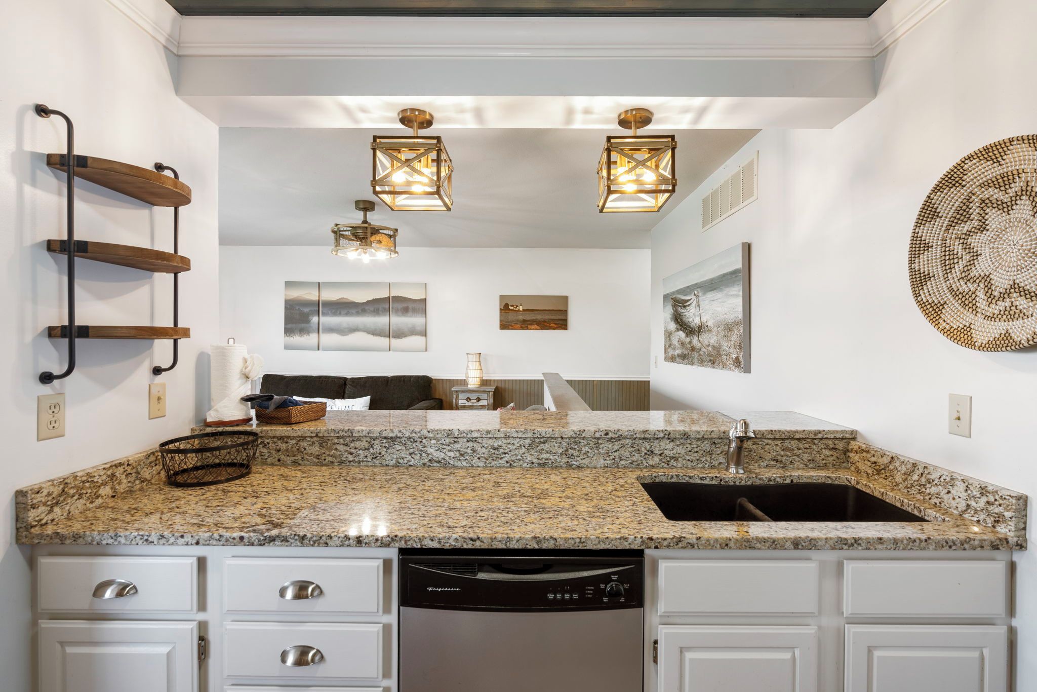A kitchen with granite countertops, a dishwasher, white cabinetry, and a hanging light fixture.