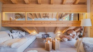 Un acogedor dormitorio tipo loft con techo inclinado, vigas de madera, un ventanal grande, un sofá, un oso de peluche y una lámpara.