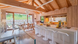 Una cocina moderna con vigas de madera, una zona de bar con taburetes y vistas a espacios verdes al exterior.