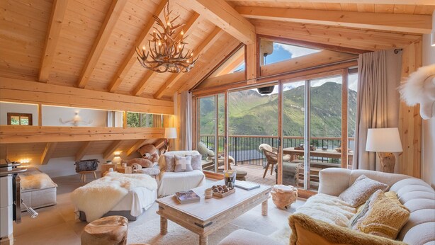 Un salón acogedor con muebles de madera y un gran ventanal con vistas a un paisaje montañoso.