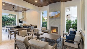 An outdoor patio area with a fireplace, seating, and a kitchen area. - Reunion's Finest | Luxury 10BR Home w Golf Course View, Private Pool, Theater and Arcade Near Disney (Kissimmee)