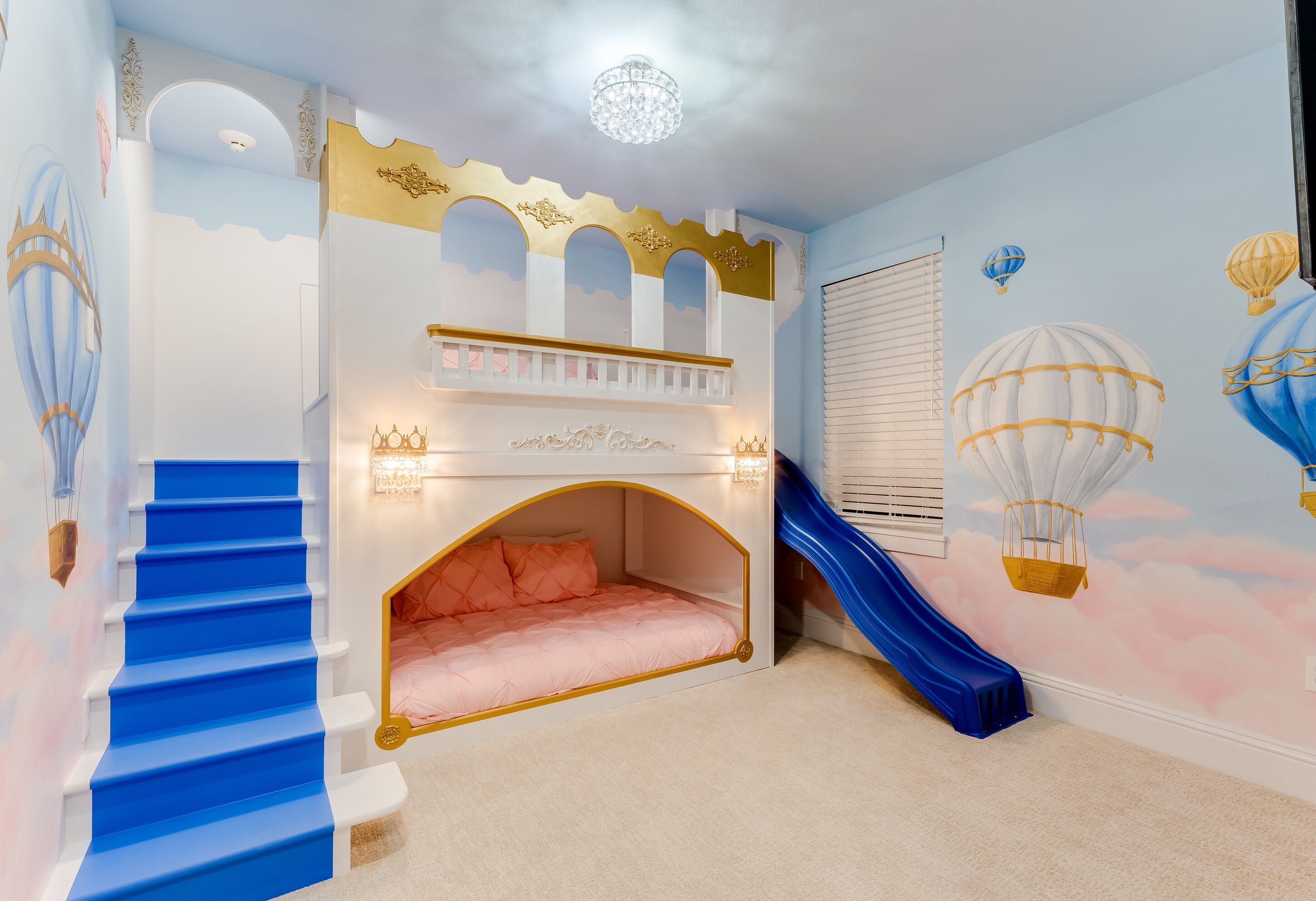 Une chambre d’enfant avec un lit superposé, un toboggan bleu et une fresque représentant des montgolfières.