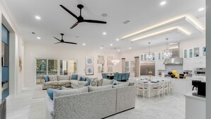 A modern living room with a sectional sofa, dining area, and kitchen. - Reunion's Finest | Luxury 10BR Home w Golf Course View, Private Pool, Theater and Arcade Near Disney (Kissimmee)