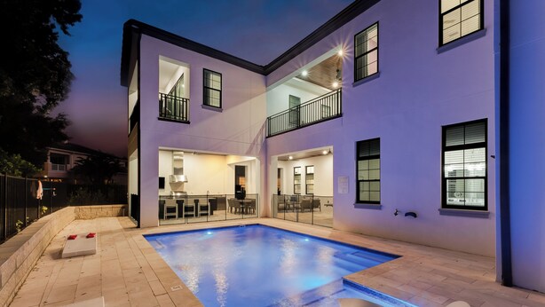 A modern building with a swimming pool, outdoor seating, and a balcony. - Reunion's Finest | Luxury 10BR Home w Golf Course View, Private Pool, Theater and Arcade Near Disney (Kissimmee)