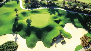 An aerial view of a golf course with sand bunkers, palm trees, and a well-maintained green. - Reunite at Reunion | 3BR, 3 Bath Spacious Condo w/ Golf Course Views Near Disney (Kissimmee)
