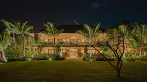 A large, well-lit hotel with a symmetrical facade, multiple balconies, and a manicured lawn with palm trees.