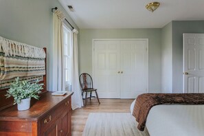 Une chambre à coucher avec un lit, une commode, une chaise, une porte et une fenêtre avec des rideaux.