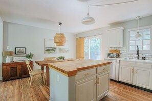 Une cuisine moderne avec des meubles blancs, un îlot central en bois et des luminaires suspendus.