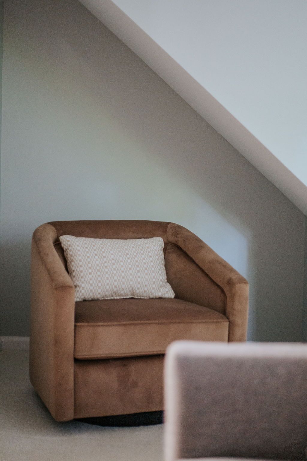 Un fauteuil marron avec un coussin à motifs, dans une pièce dont le plafond est en pente.