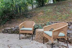 Two wicker chairs with cushions, placed on a concrete surface with a stone wall and greenery in the background. - Stuart Cottage: Walk to downtown + Sleeps 8 (Staunton)