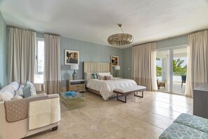 A spacious bedroom with a large bed, a bedside table, a chair, and a glass coffee table.